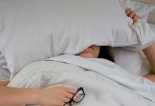 “하루 종일 피곤한데 병원에선 이상 없다?” person lying on bed while covering face with pillow and holding eyeglasses