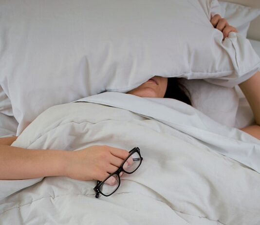 “하루 종일 피곤한데 병원에선 이상 없다?” person lying on bed while covering face with pillow and holding eyeglasses