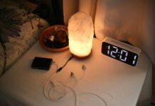 “슬립테크”와 함께 깊은 잠에 빠지다…수면 건강 관리법 Nightstand with a lamp, clock, and chargers.